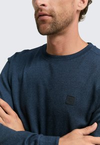Donkerblauwe sweatshirt met ronde hals, gemaakt van een gestructureerde stof, met een klein zwart logopatch op de borst en geribde manchetten.