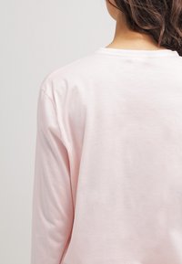 Camisa de manga larga de color rosa claro, fabricada en algodón suave, con cuello redondo, costuras mínimas, textura suave, sin patrones ni acentos visibles.