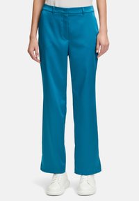 Teal vida byxor med vida ben i ett mjukt tyg med fickor, med en slät framsida och bältesöglor, bärs med vita sneakers.