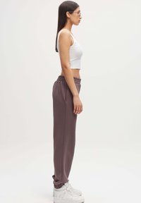 Witte geribde crop top en paarse sweatpants met een elastische tailleband, gecombineerd met witte high-top sneakers, bekeken vanuit de zijkant.