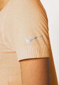 Světle oranžové atletické tričko s texturovaným síťovaným tělem a žebrovanými rukávy; na rameni je stříbrné logo Nike.