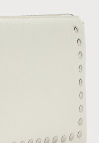 Pochette in pelle bianca testurizzata con una zip argentata e una fila di borchie metalliche circolari lungo un lato.