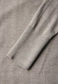 Beige tröja med en slät textur och ribbade ärmar och nederkant. Materialet verkar mjukt och mysigt, lämpligt för avslappnad användning.