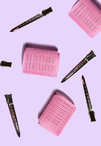 Rodillos para el cabello de color rosa con superficies texturizadas y clips metálicos esparcidos sobre un fondo lavanda. Los clips son de tono plateado y cuentan con características de agarre.