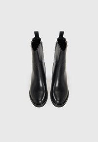 Bottines en cuir noir avec une texture lisse, bout rond, zips latéraux et languettes arrière pour un enfilage facile.