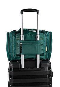 Maleta con ruedas en negro con superficie texturizada, rematada por una bolsa de tela verde con un bolsillo frontal con cremallera y asas dobles.