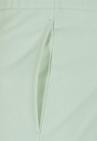 Tela de algodón verde claro con un bolsillo en la costura lateral. Textura suave con un ligero estiramiento. Diseño simple y minimalista sin patrones ni acentos.