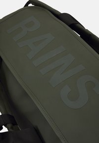 Grønn vanntett ryggsekk med matt overflate, med stort preget "RAINS"-logo, svarte stropper og sømdetaljer.