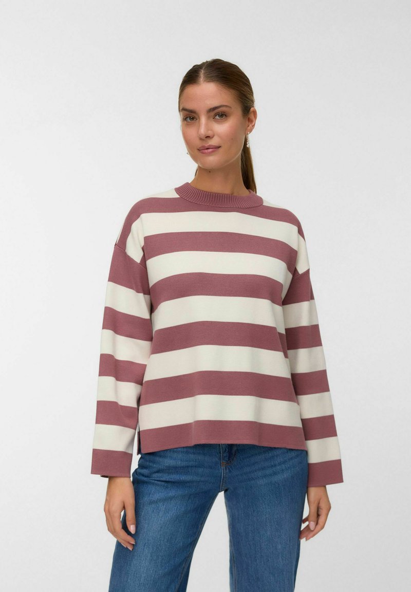 Šviesiai kreminis dryžuotas megztinis su tamsiai raudonomis horizontaliomis juostelėmis. Yra apvali iškirptė ir ilgos rankovės; medžiaga atrodo minkšta ir megzta.