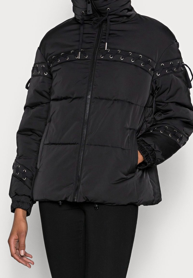 Giacca a vento nera con zip, cappuccio regolabile e dettagli a occhiello. Presenta polsini elasticizzati e tasche laterali, con texture trapuntata.