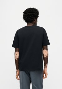 Μαύρο βαμβακερό μπλουζάκι με στρογγυλή λαιμόκοψη, κοντά μανίκια και άνετη εφαρμογή. Το ύφασμα φαίνεται απαλό και λείο, χωρίς ορατά σχέδια.