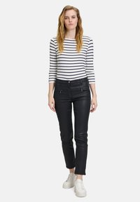 Schwarze Kunstlederhosen mit Slim-Fit. Kombiniert mit einem langärmeligen Hemd in Weiß und Marineblau mit Streifen und weißen Sneakers.