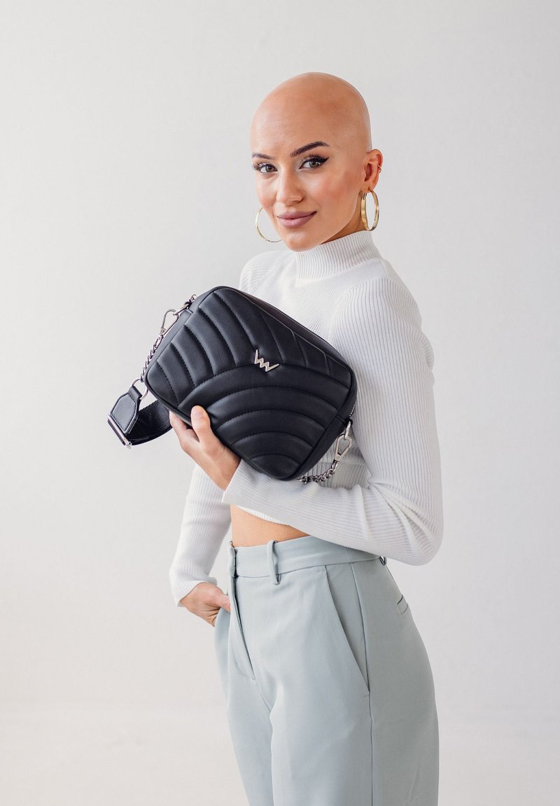 Prošívaná černá crossbody taška se stříbrným logem, obsahující řetízkový popruh a obdélníkový tvar. Hladká, umělá kůže.