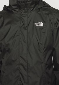 Veste imperméable noire avec une fermeture éclair à l'avant, un col haut, une capuche ajustable et le logo The North Face en blanc sur le côté gauche de la poitrine.