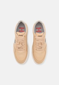 Baskets beiges avec une tige en cuir lisse, accents en daim contrastants, bout rond et lacets plats. Comprend un logo sur la languette et le talon.