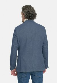 Blazer de cuadros azules hecho de tela texturizada, con una abertura simple, solapas muesca y puños abotonados, usado sobre denim.