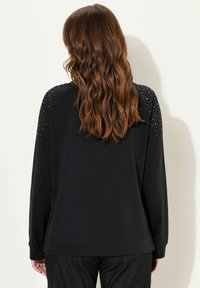 Sudadera negra de manga larga, con un diseño texturizado y con tachuelas en los hombros. Tejido suave, corte relajado y dobladillo de canalé.