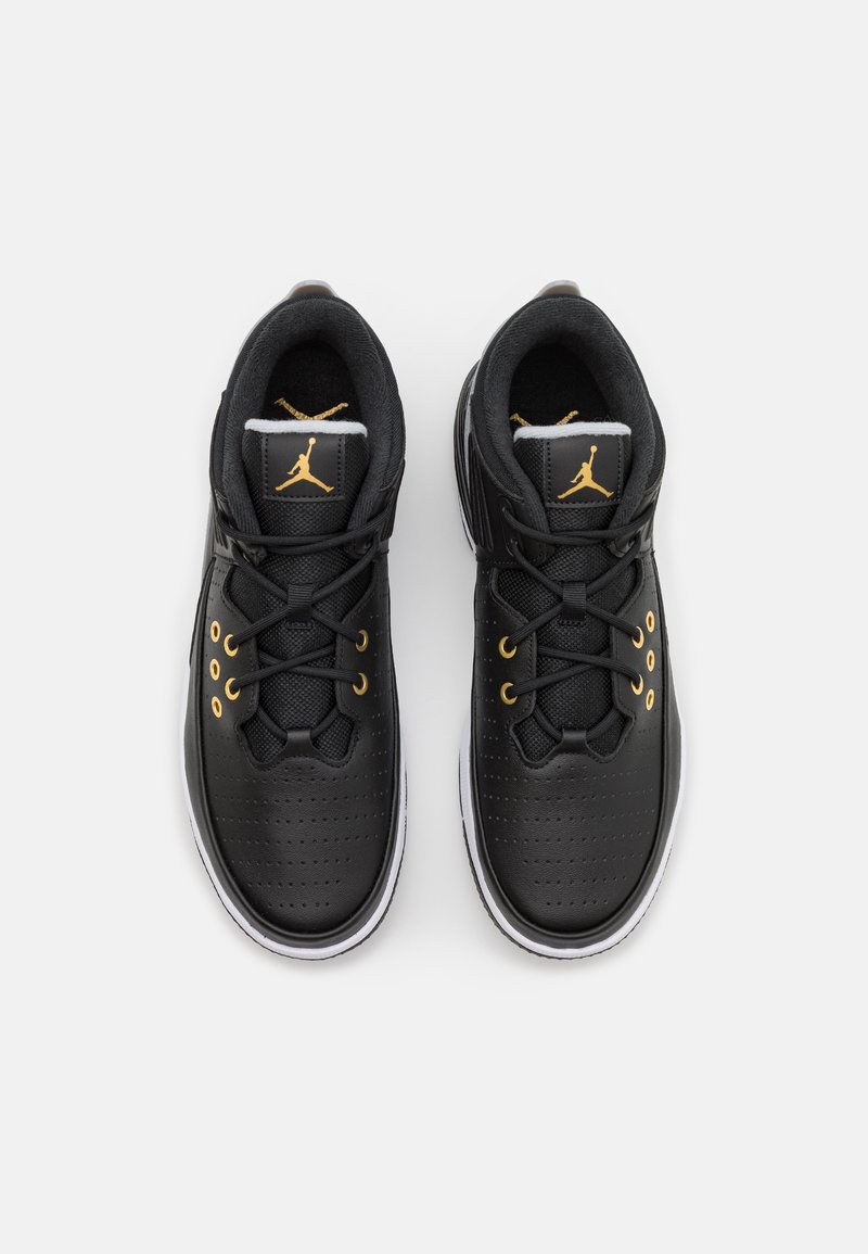 Schwarze Sportschuhe mit einem glatten Lederobermaterial, goldenen Akzenten, Perforationen und einer weißen Gummisohle. Ausgestattet mit schwarzen Schnürsenkeln und einem Logo.