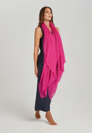 Sciarpa oversize fucsia realizzata in materiale leggero, con orlo frangiato e design drappeggiato, indossata sopra un outfit nero.