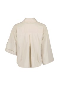 Camicia beige a maniche corte con colletto, dettaglio della piega sul retro e una vestibilità ampia. Realizzata in tessuto liscio con un design snodato.