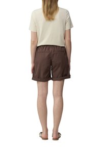T-shirt beige clair, à manches courtes, associé à un short marron de longueur genou avec une taille élastique et des poignets retroussés. Porté avec des sandales.