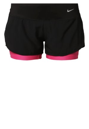 Vrouw draagt een zwarte Nike tanktop, zwarte shorts met roze ondershorts en zwarte Nike sneakers, lopend vooruit tegen een effen achtergrond.