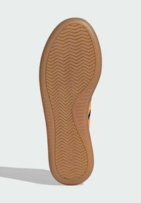 Sole of a shoe featuring a gum rubber material, textured with a zigzag pattern. The edge curves smoothly, with embossed branding.