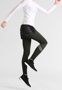 Svart kort över mörkgröna leggings, en figurnära vit långärmad topp och svarta sportskor med vita sulor; har reflekterande ränder.