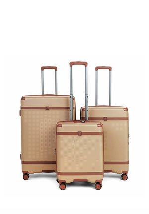 Tre valigie rigide beige con quattro ruote e maniglie telescopiche estese, di dimensioni diverse, disposte affiancate su sfondo bianco.