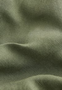 Olivgrüner, gewebter Stoff mit sichtbarer Textur und kleinem, gleichmäßigem Rautenmuster, dargestellt in sanften Falten und Beleuchtung.