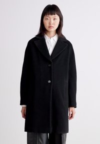 Schwarzer Wollmantel mit Reverskragen, Ein-Knopf-Verschluss, seitlichen Taschen und lockerem Schnitt. Glatte Textur und minimalistisches Design.