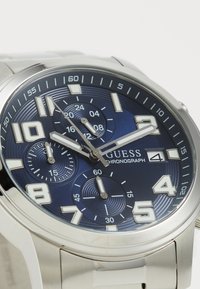 Reloj de acero inoxidable plateado con un dial texturizado azul, marcadores de horas blancos, sub-diales de cronógrafo y una pantalla de fecha a las 4 en punto.