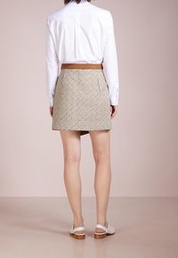 Una falda marrón con un diseño estampado y plisado, combinada con una camisa blanca y un cinturón marrón, acompañada de sandalias blancas con tacones de madera.