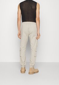 Světlé béžové cargo kalhoty s elastickým pasem, bočními kapsami a zúženými manžetami. Nositelný s černým tílkem bez rukávů a hnědými botami.