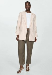 Light pink oversized blazer, white t-shirt, and olive green drawstring pants. Strappy white heels. Smooth fabric, relaxed fit.