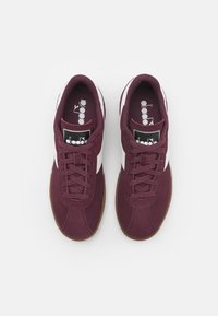 Bordové tenisky s bílými akcenty, šněrovací design, textura podobná semiši, zaoblená špička a gumová podrážka. Logo značky na jazyku.