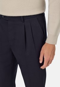 Jūras spēku bikses ar krokām, izgatavotas no gludas auduma, piedāvā sānu kabatas un pogu aizdari. Akcentētas ar kontrastējošu beidzzi svīteru.