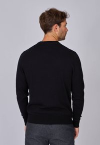 Pull en tricot noir avec un col rond et des manches longues, présentant des poignets et un ourlet côtelés. Texture lisse, design minimal.