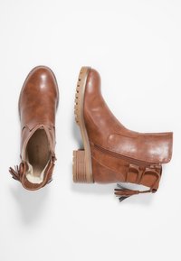 Bottes chelsey en cuir marron avec un petit talon bloc, fermeture éclair sur le côté et franges décoratives. Présentent une surface texturée et un bout rond.