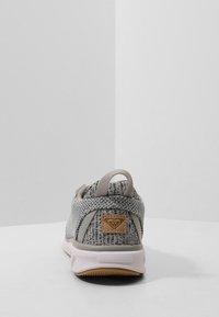 Baskets en maille grise avec une tige texturée, un col rembourré, des accents beige et une semelle en caoutchouc. Comprend un patch logo sur le talon.