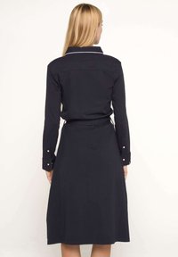 Robe noire à manches longues, avec col et ceinture. Présente des poignets boutonnés et un tissu lisse et texturé. Design simple et classique.