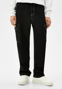 Svarta cargobyxor med vit söm, sidofickor, avslappnad passform och en mjuk yta, i kombination med vita sneakers.