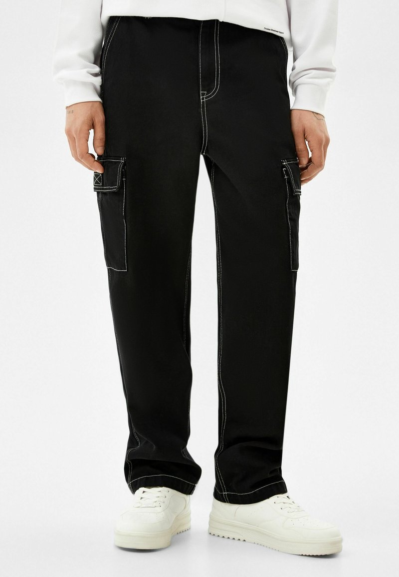 Svarta cargobyxor med vit söm, sidofickor, avslappnad passform och en mjuk yta, i kombination med vita sneakers.