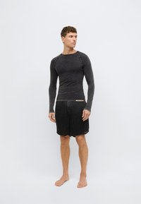 Čierny top s dlhým rukávom a okrúhlym výstrihom s kontrastnými švami, v kombinácii s čiernymi riflovými šortkami s rozstrapateným lemom a zapínaním na gombíky.