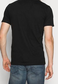 Svart kortärmad t-shirt med klassisk rund halsringning, tillverkad av mjuk bomull, som bärs med ljusblå denimjeans med böjda bakfickor.