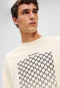 Crème sweatshirt met een ronde hals, met een zwart geometrisch patroon en het "Karl Lagerfeld" logo bovenaan. Zachte katoenmix materiaal.