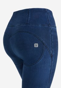 Jeans de tiro alto de color azul oscuro con una textura suave, que presentan costuras curvas y un pequeño parche con el logo en el bolsillo trasero.