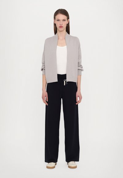 Svetlo siva bomber jakna s okruglim izrezom, crne široke hlače i kremasti patiki. Jednostavan, minimalistički dizajn s opuštenim krojem.