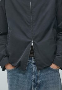 Marineblaue leichte Jacke mit Frontreißverschluss, seitlichen Taschen und lockerem Schnitt, kombiniert mit hellblauen Jeans.