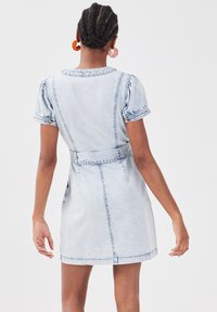 Light blue denim dress with short puff sleeves, belted waist, and back pockets. Features stitching accents and a rounded neckline.
